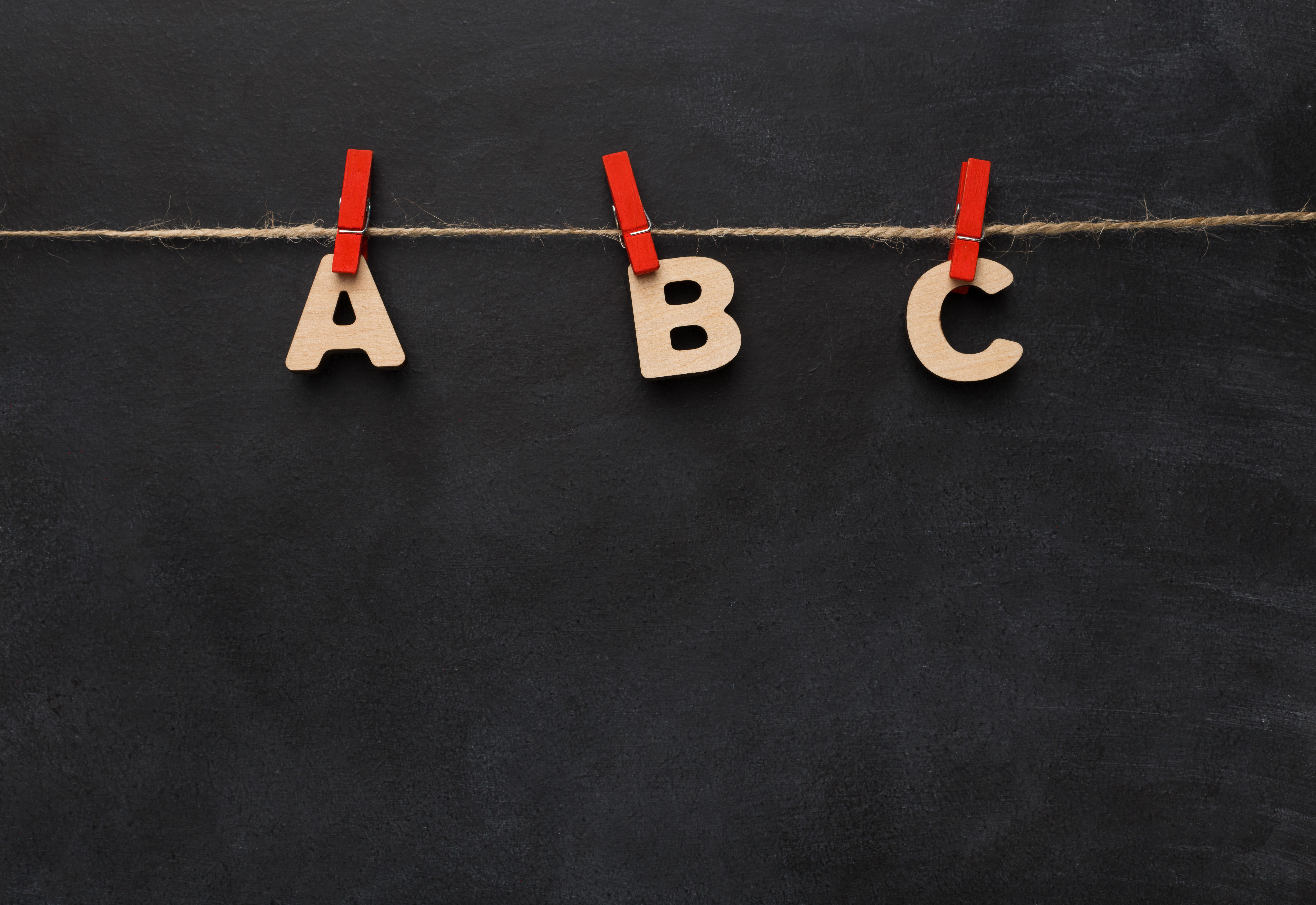 Back to school concept. Alphabet ABC made of wooden letters handing on clothespins on black background, top view, copy space